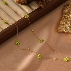 Macro détaillée d'un collier doré avec breloques fleurs perlées vertes et billes d'or