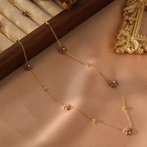 Collier élégant en acier doré avec perles de fleurs violettes sur fond de soie douce