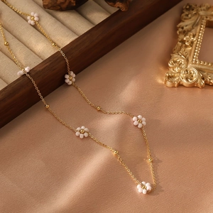 Détail d'un collier en chaîne dorée avec des perles florales roses et blanches sur soie