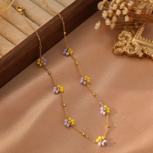 Détail d'un collier doré avec fleurs perlées mauves et jaunes sur tissu en soie champagne