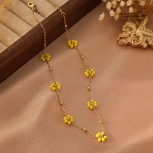 Détail d'un collier en acier doré avec fleurs en perles jaunes sur soie rose