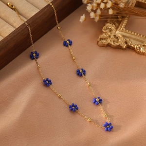 Détail de collier chaîne dorée orné de petites fleurs délicates en perles bleues