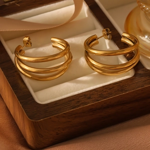 Detail of three-layer gold C-shaped earrings on white velvet in a walnut box