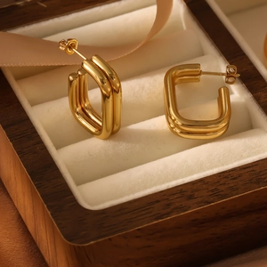 Macro shot of gold geometric square hoop earrings on a velvet display in a jewelry box