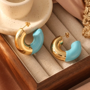 Polished gold and sky blue enamel C-shape hoop earrings on a minimalist wooden display box