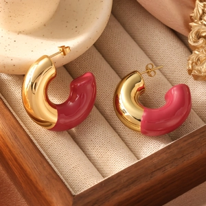 Close-up of gold-plated C-shaped earrings with magenta enamel finish on velvet