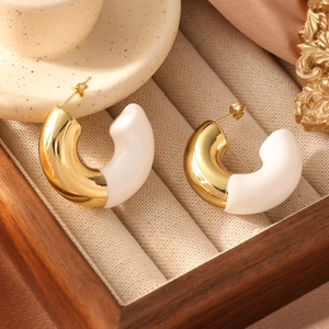 Detail view of gold C-shape enamel earrings displayed in a luxury wooden jewelry box