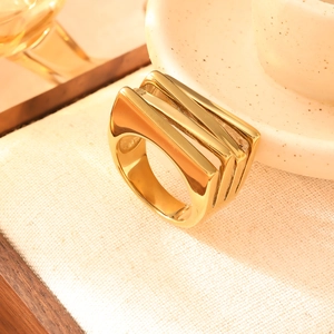 Anello multistrato moderno in acciaio inossidabile dorato su sfondo di tessuto beige