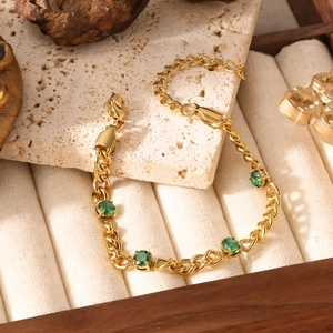Gold rope chain bracelet with four prong-set green gemstones on a beige stone surface