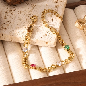 Detail of gold chain bracelet with oval links and four colored gemstones on stone base