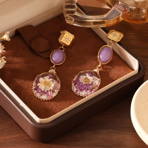Close-up of dried flower drop earrings with purple gems in a brown jewelry box