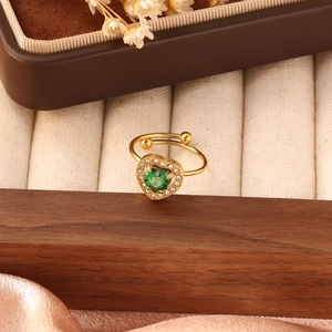 Dettaglio anello dorato regolabile con pietra a cuore verde e zirconi su legno