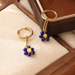 Détail de boucles d'oreilles fleur en perles bleues avec anneau doré sur fond vintage