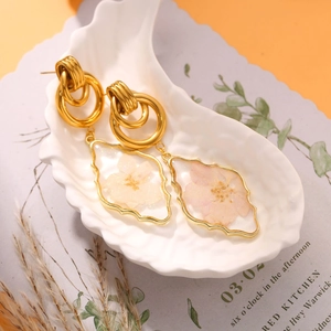 Handmade teardrop earrings with pink dried flowers in gold rings on a shell tray