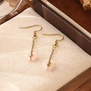 Gros plan sur les boucles d'oreilles fleurs roses mates avec crochets dorés sur lin beige