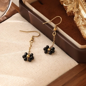 Détail des boucles d'oreilles bohèmes tissées en fleurs avec perles noires et crochets d'or