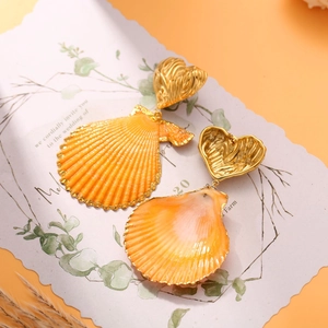 Close-up of golden heart-shaped shell drop earrings on a decorative wedding invite card