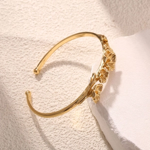 Macro detail of golden plum blossom branch cuff bracelet on a white textured stone base