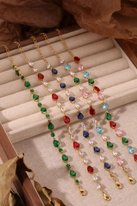 Détail de bracelets chaîne dorée avec zircons colorés taille poire sur velours beige