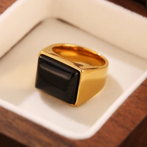 Gros plan d'une bague chevalière vintage dorée avec une grande pierre noire carrée en boîte