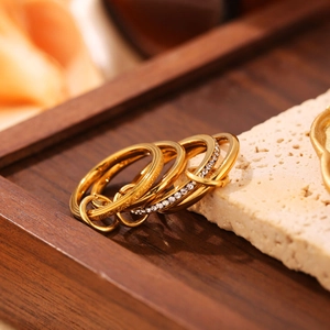 Dettaglio di quattro anelli d'oro impilati con zirconi incastonati su travertino e legno