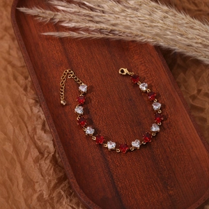 Bracelet doré élégant avec zircons en forme de cœur rouges et blancs sur bois