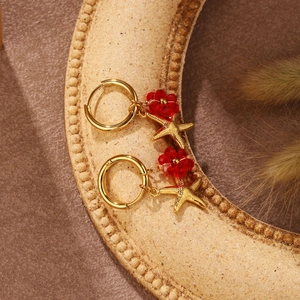 Detail von goldenen Creolen mit roten Blumenperlen und Seestern-Anhängern für Damen