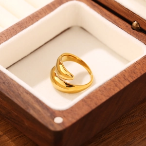 Anello avvolgente dorato a goccia lucido a specchio su espositore in legno di noce