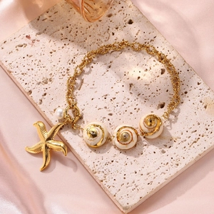 Goldenes Seestern- und Muschel-Armband mit weißer Perle auf beigem Travertinstein