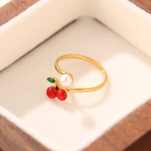 Dettaglio di un anello d'oro aperto con ciondolo a ciliegia rossa e perla bianca lucida