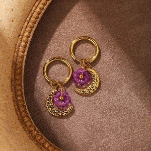 Macro detail of gold crescent moon and purple beaded flower drop earrings on felt texture