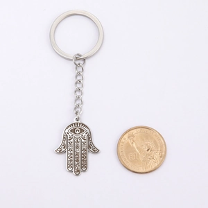Detail of Hamsa Hand keychain with evil eye design next to coin for size scale