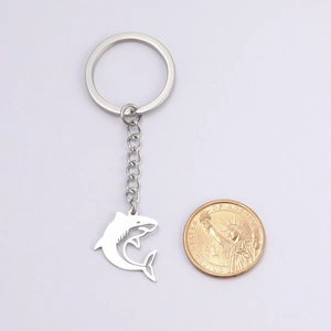 Polished stainless steel shark pendant keychain with coin for scale on white background