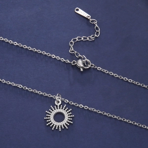 Detailed macro view of a silver sunburst pendant on a fine stainless steel chain