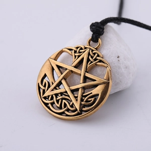 Detail shot of vintage bronze pentagram pendant on black woven rope over white pebbles