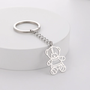 Creative hollow bear keychain in silver metal with polished chain on white pedestal