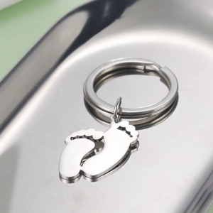 Polished stainless steel baby feet footprint keychain pendant on a metal tray