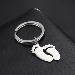 Polished stainless steel baby feet keychain charms on a black textured leather background
