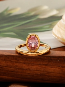 Dettaglio di un anello vintage in titanio dorato con gemma rosa ovale su supporto in legno
