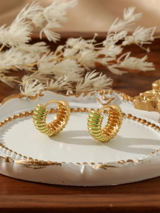 Close-up of chunky gold hoop earrings with green enamel stripes on a white ceramic tray