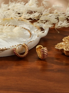 Detail of gold-plated hoop earrings featuring purple enamel stripes on a wooden surface