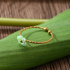 Macro detail of adjustable gold floral ring with light green frosted flower on green leaves