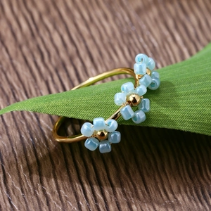Detail shot of a gold adjustable ring featuring delicate light blue beaded flowers on a leaf