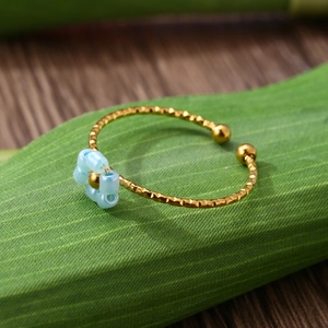 Macro detail of adjustable gold floral ring with blue beads on a green leaf