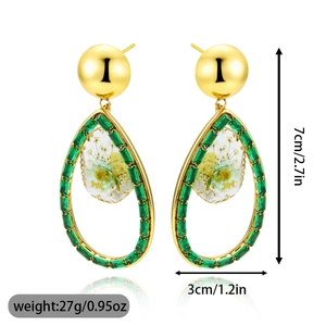 Detalle de pendientes de gota huecos con piedras verdes y colgantes de flores amarillas