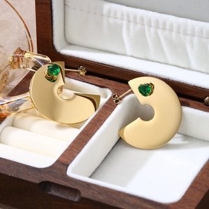 Dettaglio di orecchini a C placcati oro con pietre verdi a cuore su velluto bianco liscio