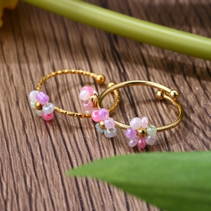 Set of two gold adjustable rings with colorful beaded flowers on natural wood