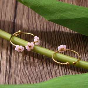 Close-up of adjustable gold rings with pink bead flowers on green leaves and wood background