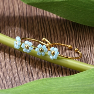 Close-up of adjustable gold rings with light blue floral beads on green plant branch