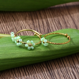 Detail of adjustable gold rings with green handmade beaded flowers in a nature-inspired style